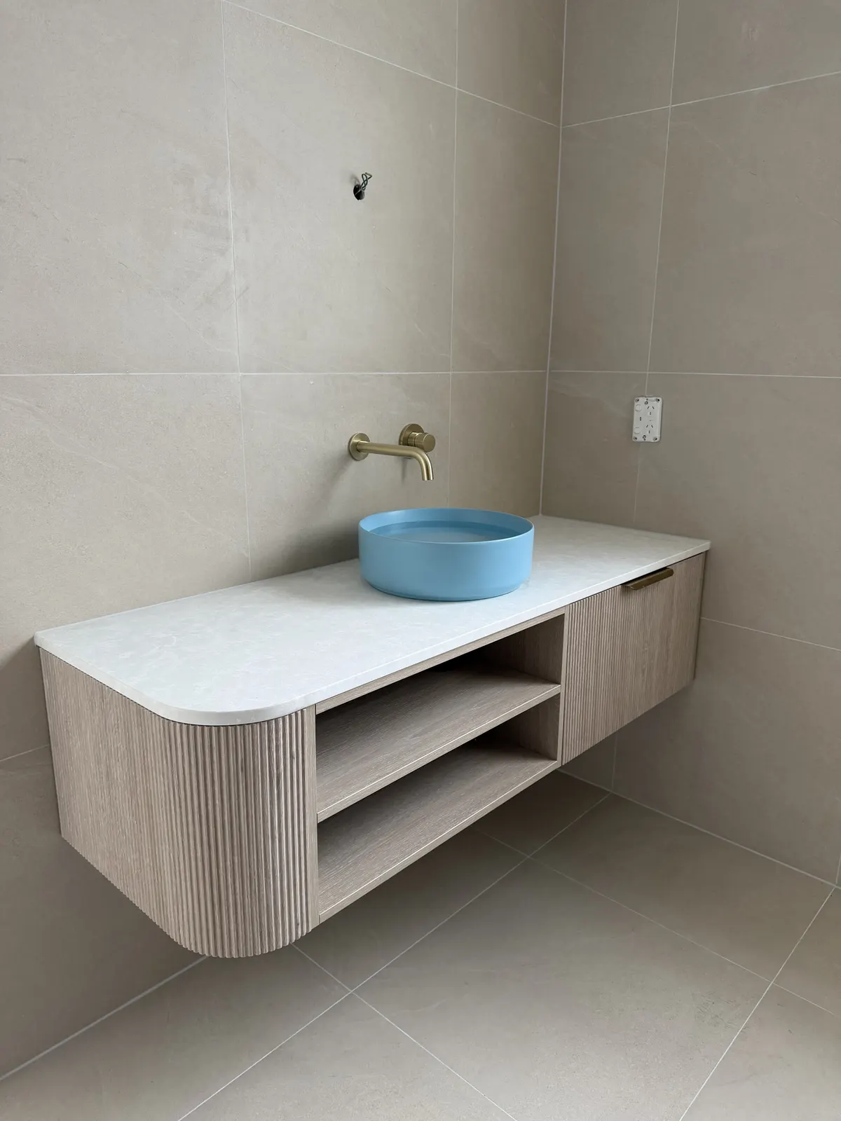 Curved fluted timber vanity with a blue vessel basin and brass wall tap