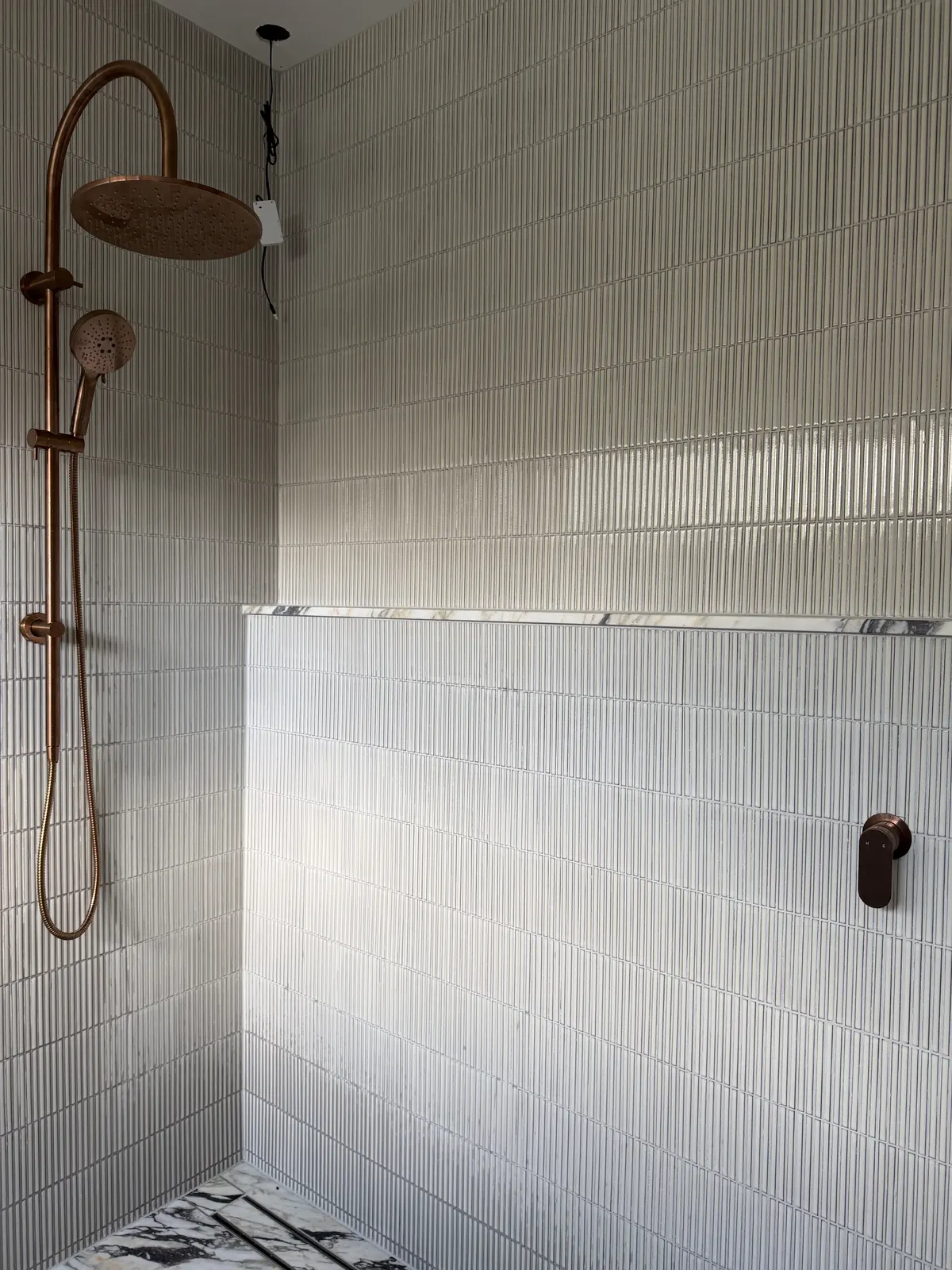 Copper rain shower and hand shower against fluted tiles