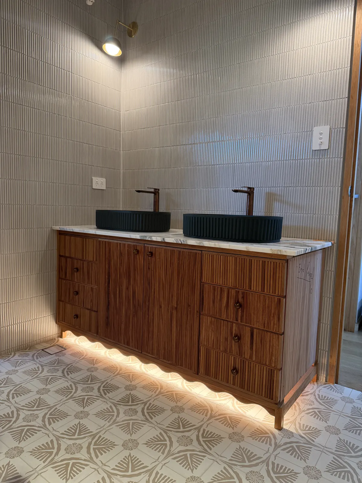 Timber double vanity with dark basins, LED under-lighting and patterned floor tiles