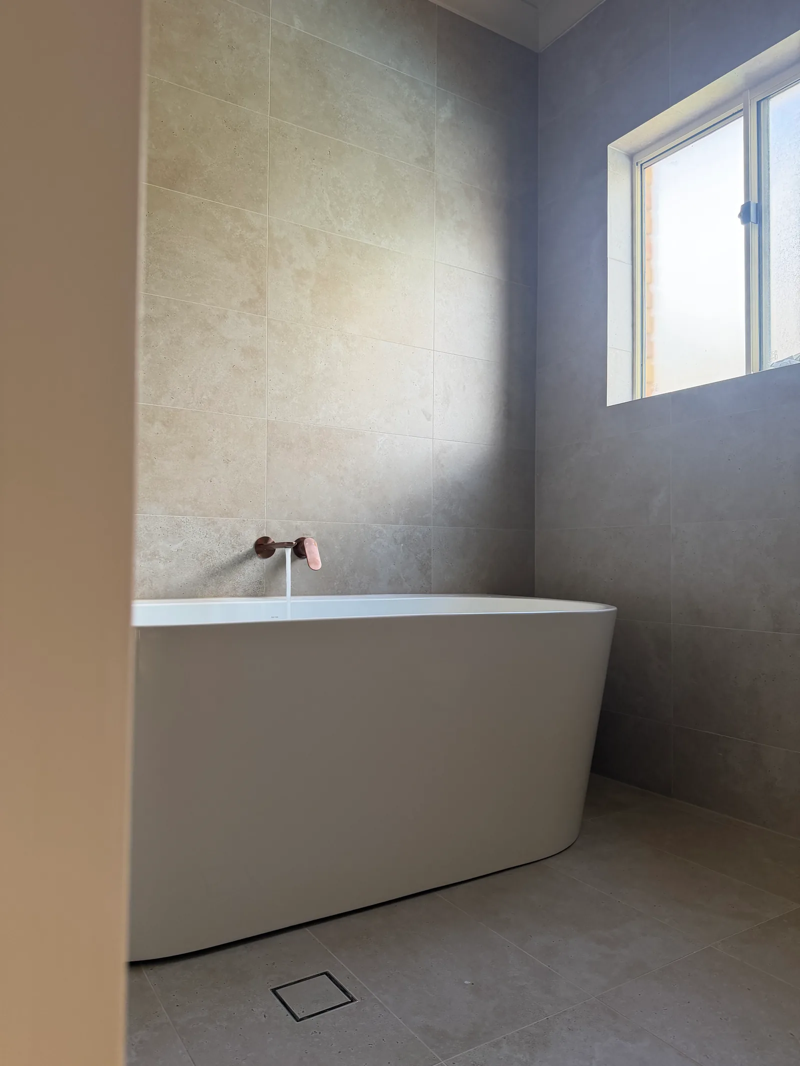 Freestanding bath beneath a window with a wall-mounted copper tap
